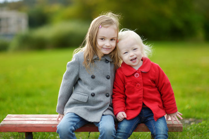 Two little sisters sitting on a park bench