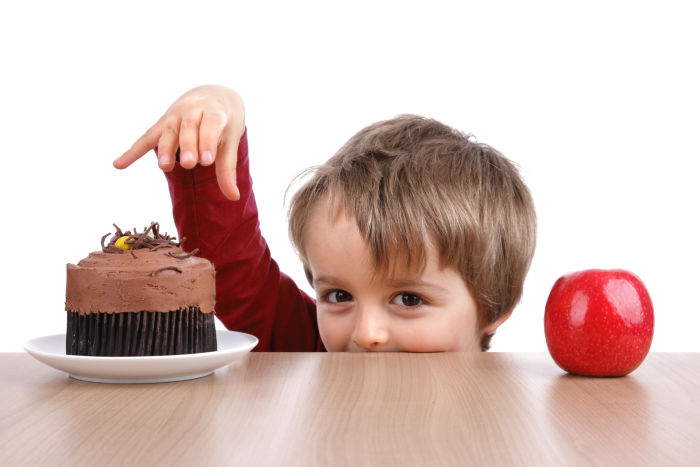 Little boy deciding between apple and cupcake
