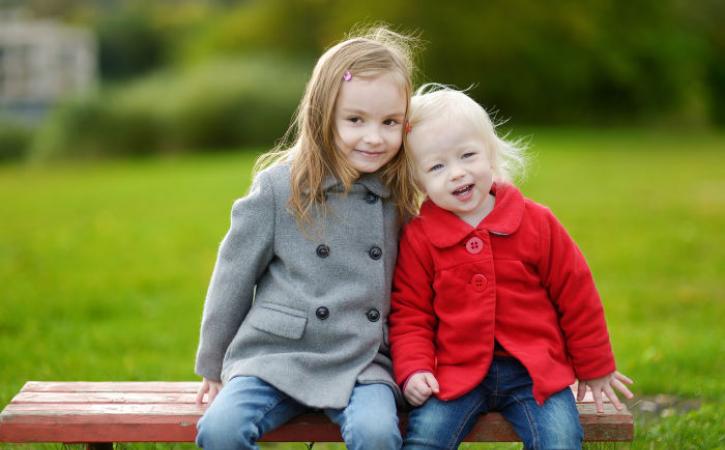 Two little sisters sitting on a park bench