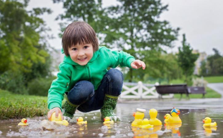 Little boy playing in puddle with rubber ducks