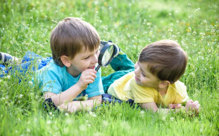 Two little boys with magnifying glass in grass